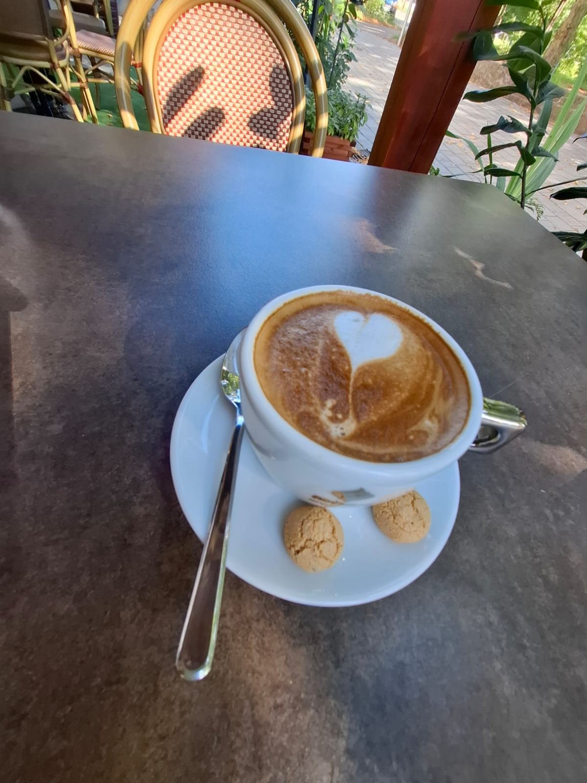 Cappuccino mit Milchschaum-Herz und Amarettini auf der Terrasse