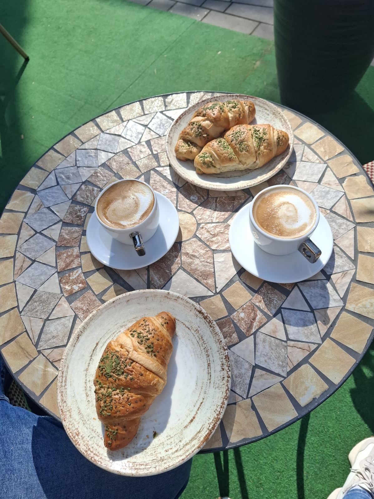 Zwei Cappuccino und Croissants auf dem Mosaiktisch in der Sonne